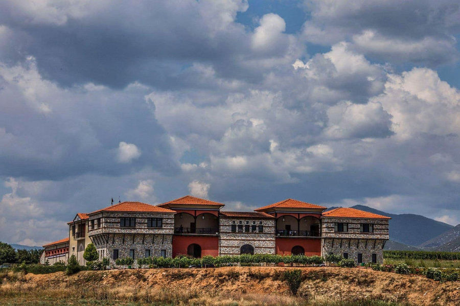 on side of 'Oenogenesis Estate' stone building surrounded by trees and blue sky in the background